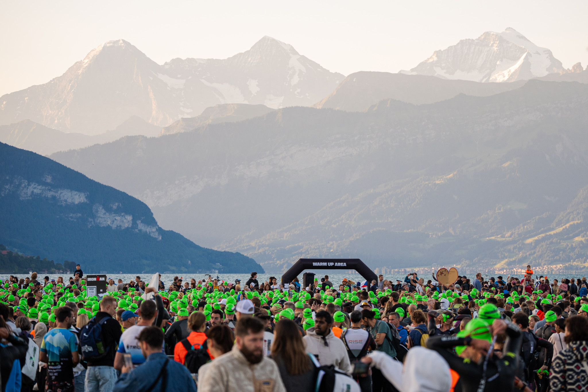 Hunderte Ironman-Athleten mit grünen Badekappen versammeln sich beim Start in Thun, im Hintergrund die schneebedeckten Berner Alpen. Hunderte Ironman-Athleten mit grünen Badekappen versammeln sich beim Start in Thun, im Hintergrund die schneebedeckten Berner Alpen.