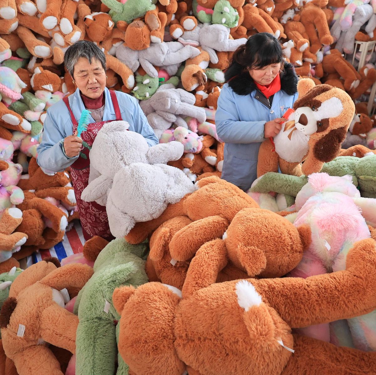 Zwei Arbeiterinnen in einer Spielzeugfabrik in der Stadt Lianyungang, China, umgeben von grossen, bunten Plüschtieren.