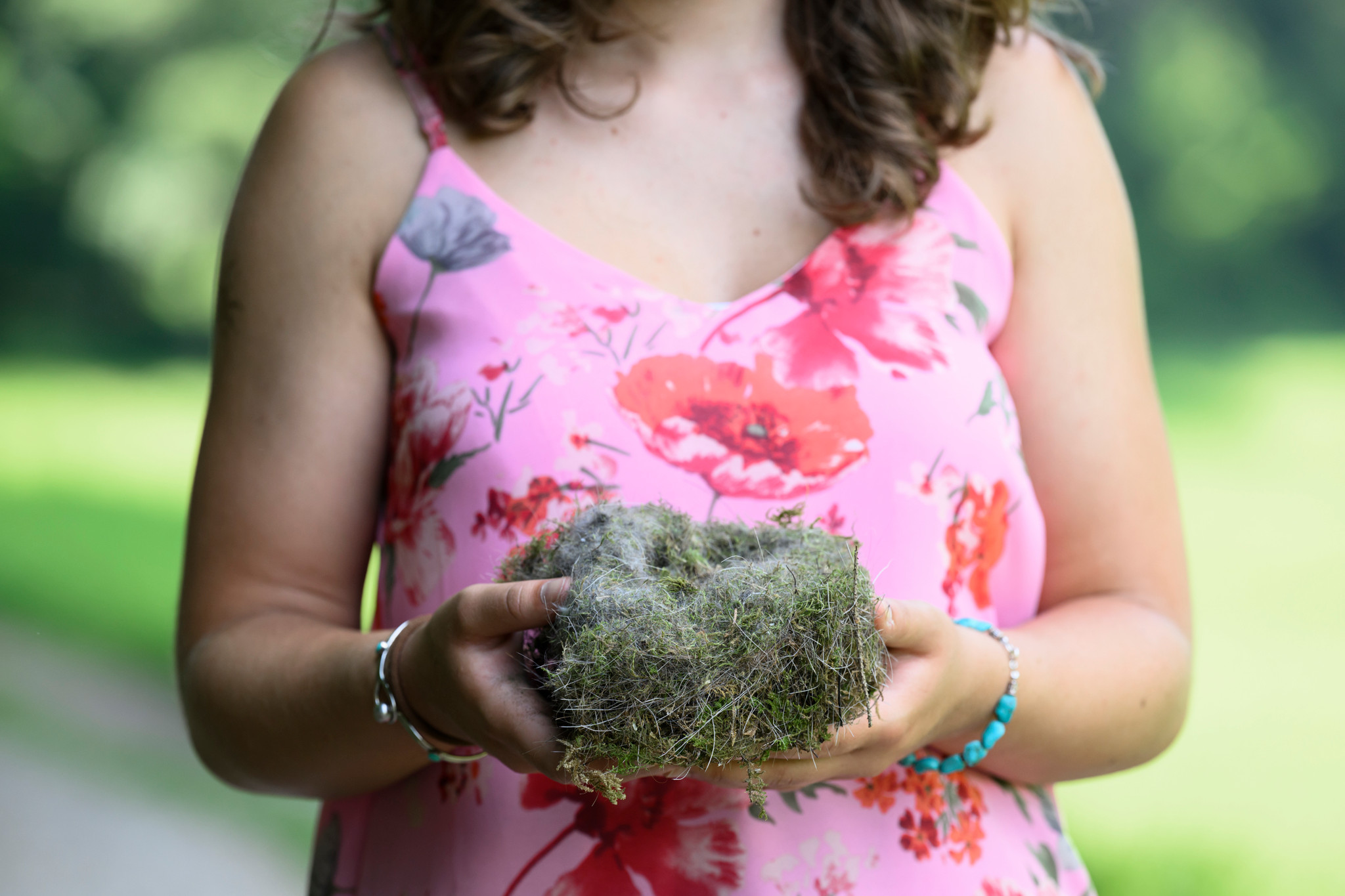 Eine junge Frau in einem blumigen Sommerkleid hält ein Vogelnest in den Händen auf dem Natur-Erlebnispfad FederFröhlich in Steffisburg.