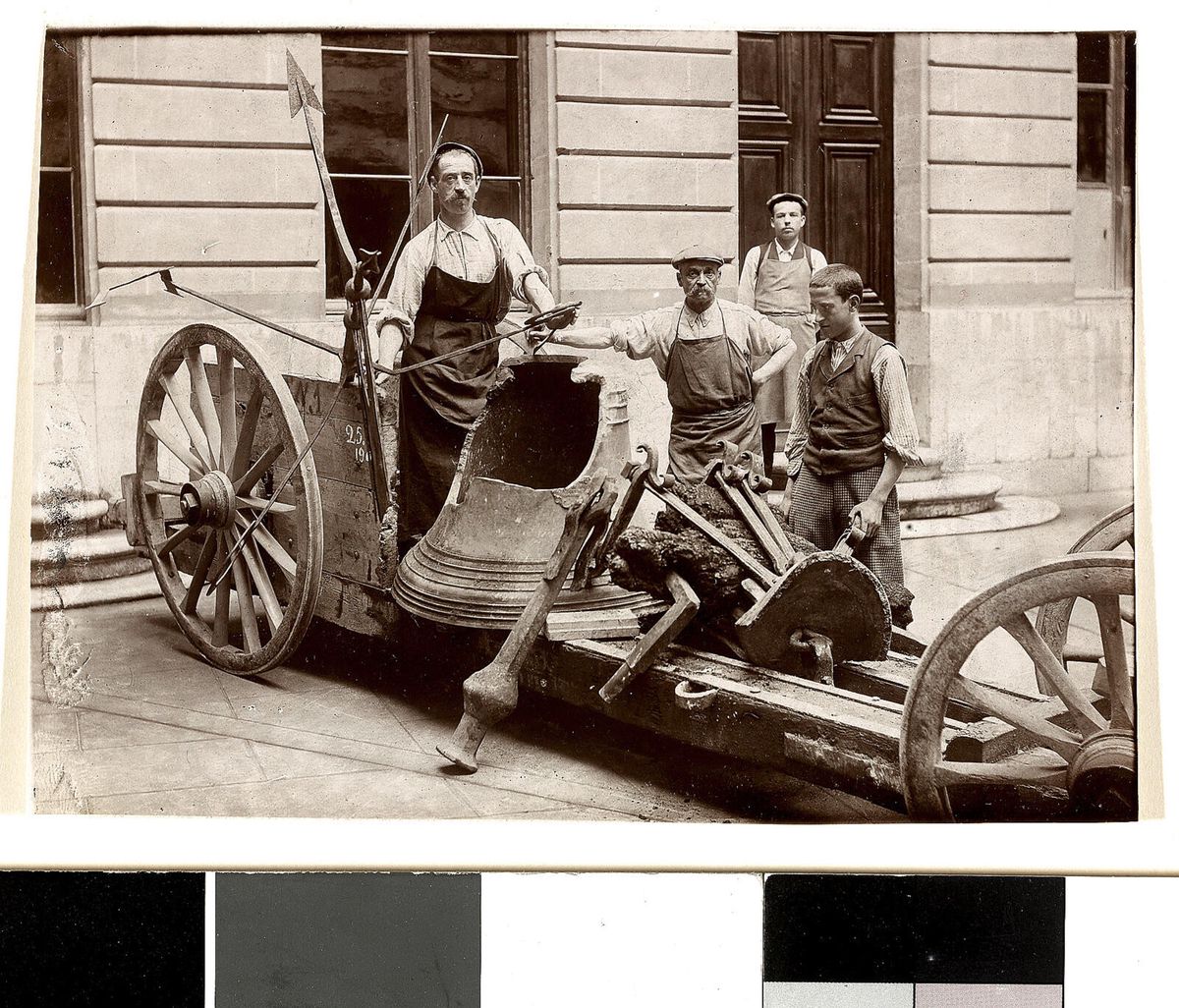 Quatre ouvriers posent autour d'une vieille machine agricole devant un bâtiment en pierre.