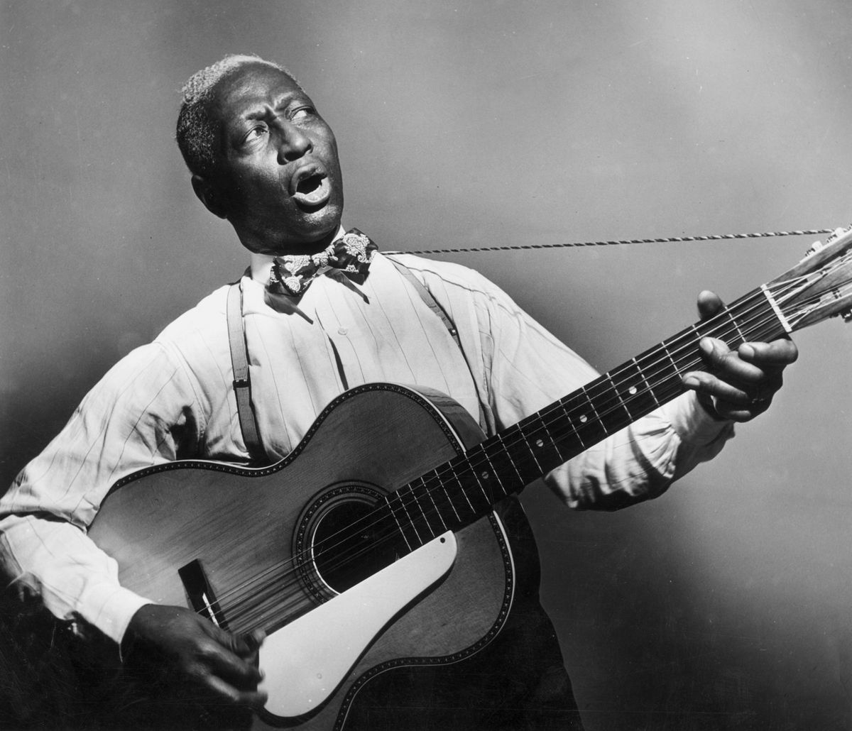 circa 1935:  Promotional portrait of American blues musician Huddie 'Leadbelly' Ledbetter (1889 - 1949) playing a 12-string guitar and singing.  (Photo by Hulton Archive/Getty Images)