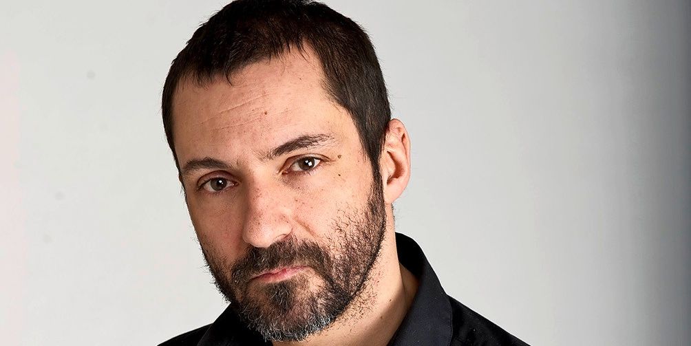 Un homme barbu en chemise noire regarde l'objectif avec une expression sérieuse.