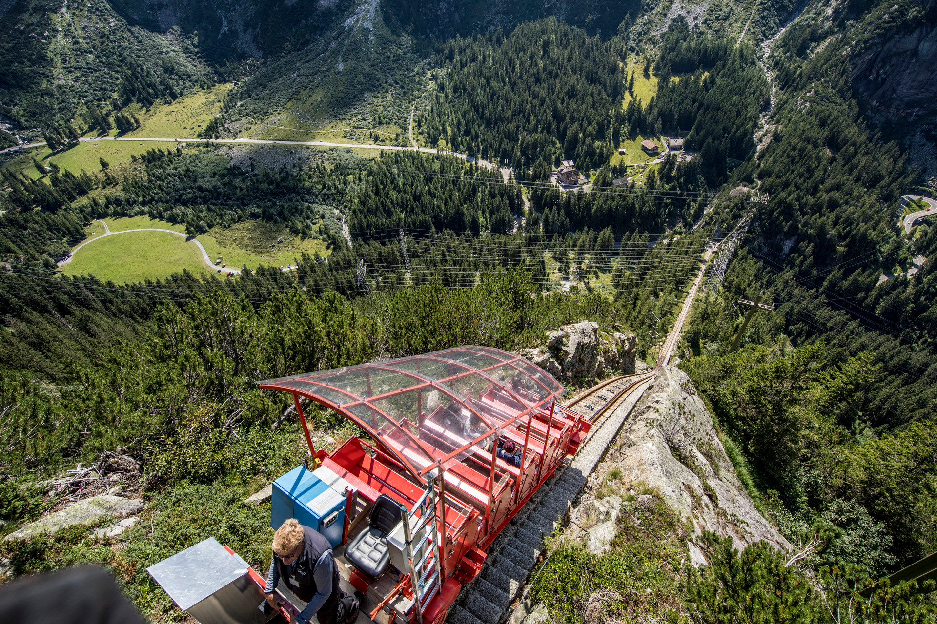 Die rote Gelmerbahn in der Grimselwelt führt steil den Felsen hinab, im Hintergrund ein grünes Alpental mit Wäldern. Die rote Gelmerbahn in der Grimselwelt führt steil den Felsen hinab, im Hintergrund ein grünes Alpental mit Wäldern.