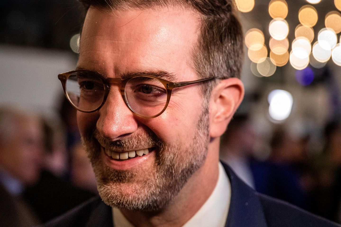 Ein Mann in Anzug und Krawatte lächelt unter festlicher Beleuchtung am Wahlsonntag in Basel-Stadt.