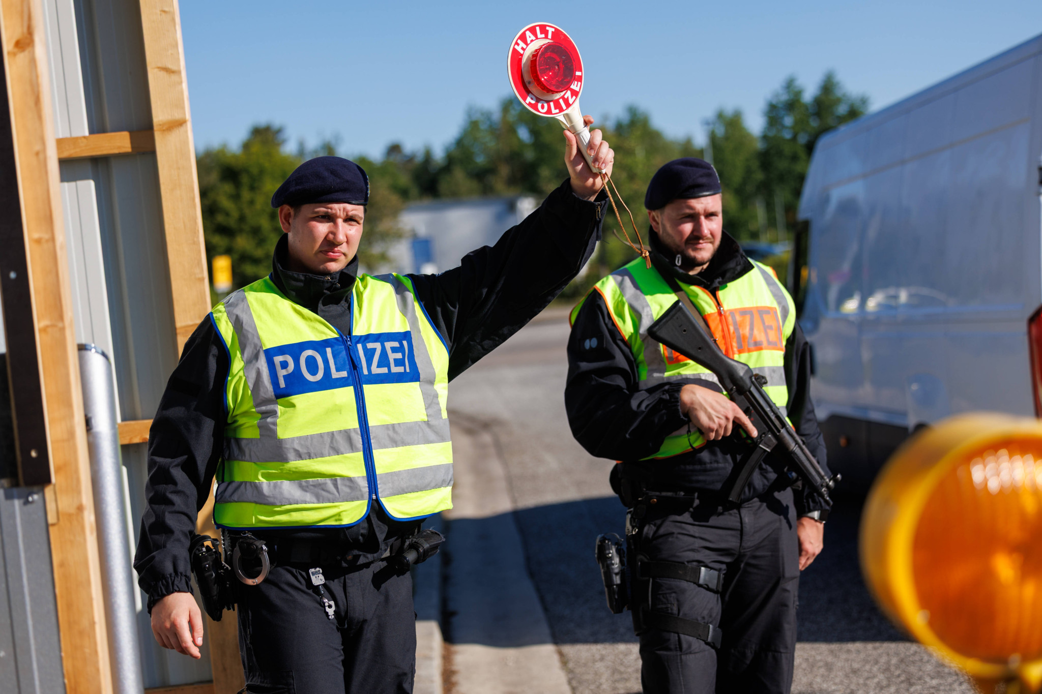 Zwei Polizisten in Warnwesten führen am 20. Mai 2025 Grenzkontrollen in Pomellen, Mecklenburg-Vorpommern, durch. Einer hält ein Schild mit ’Halt’.