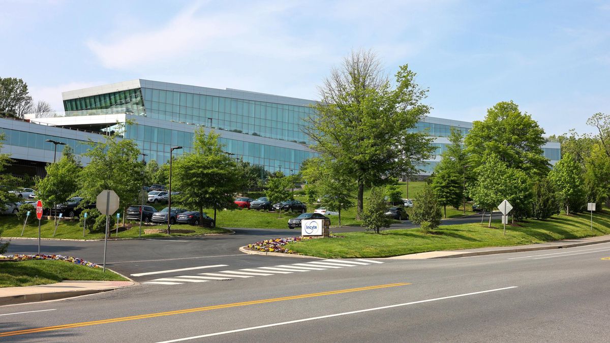 Moderner Bürokomplex mit Glasfassade, umgeben von Bäumen und einem Parkplatz, an einem sonnigen Tag.