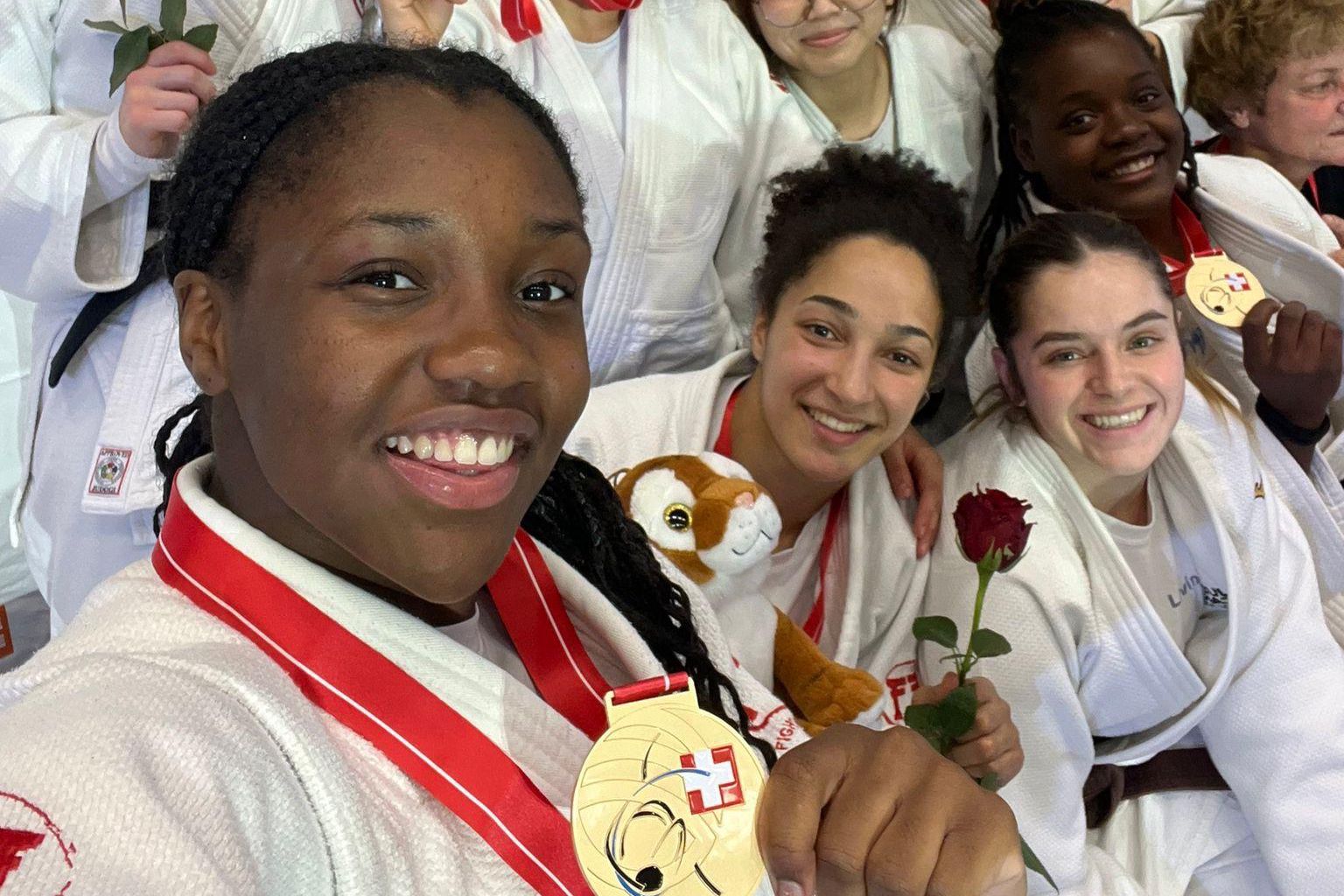 Groupe de judokas féminines souriantes, en kimono blanc, montrant leurs médailles et tenant des roses rouges.