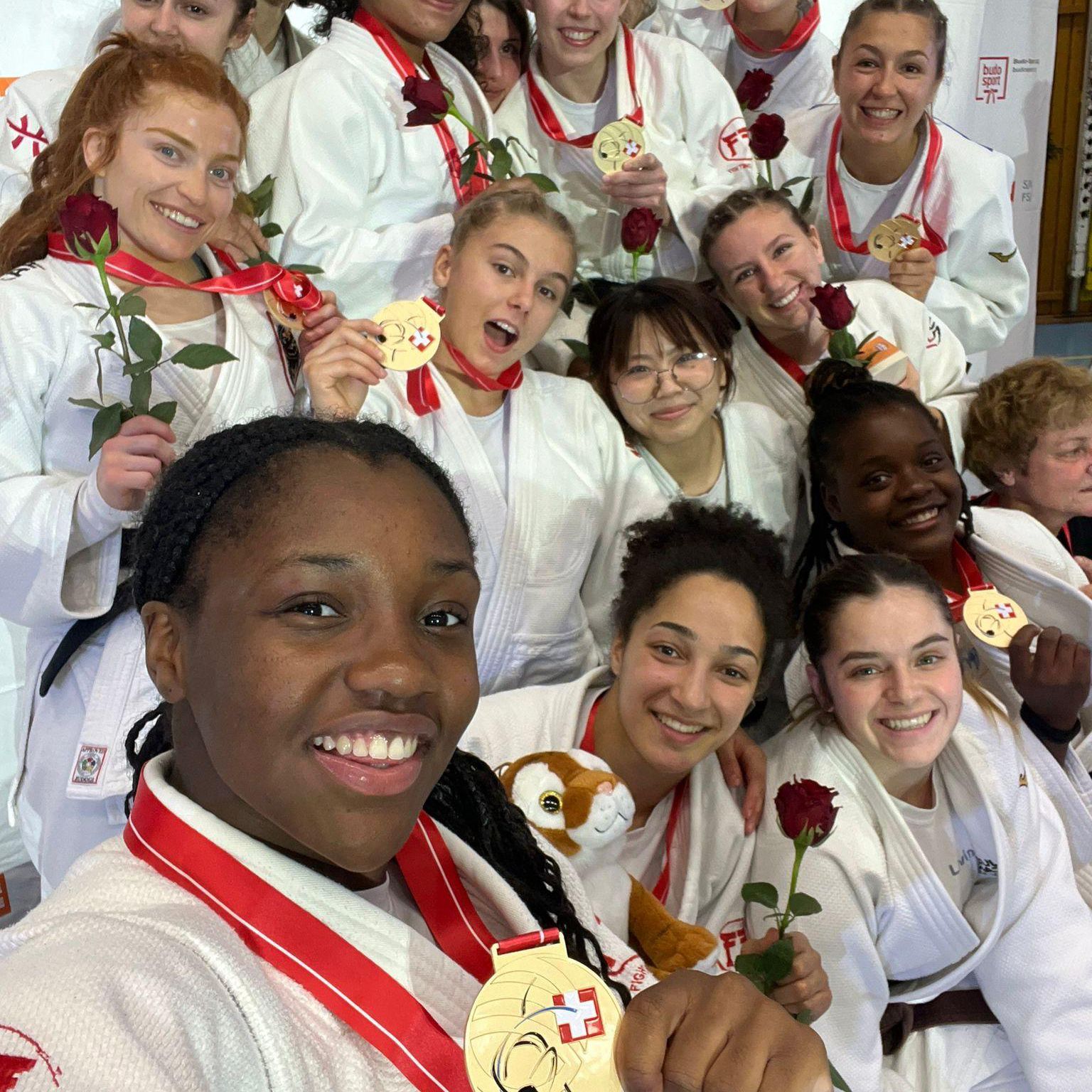 Groupe de judokas féminines souriantes, en kimono blanc, montrant leurs médailles et tenant des roses rouges.
