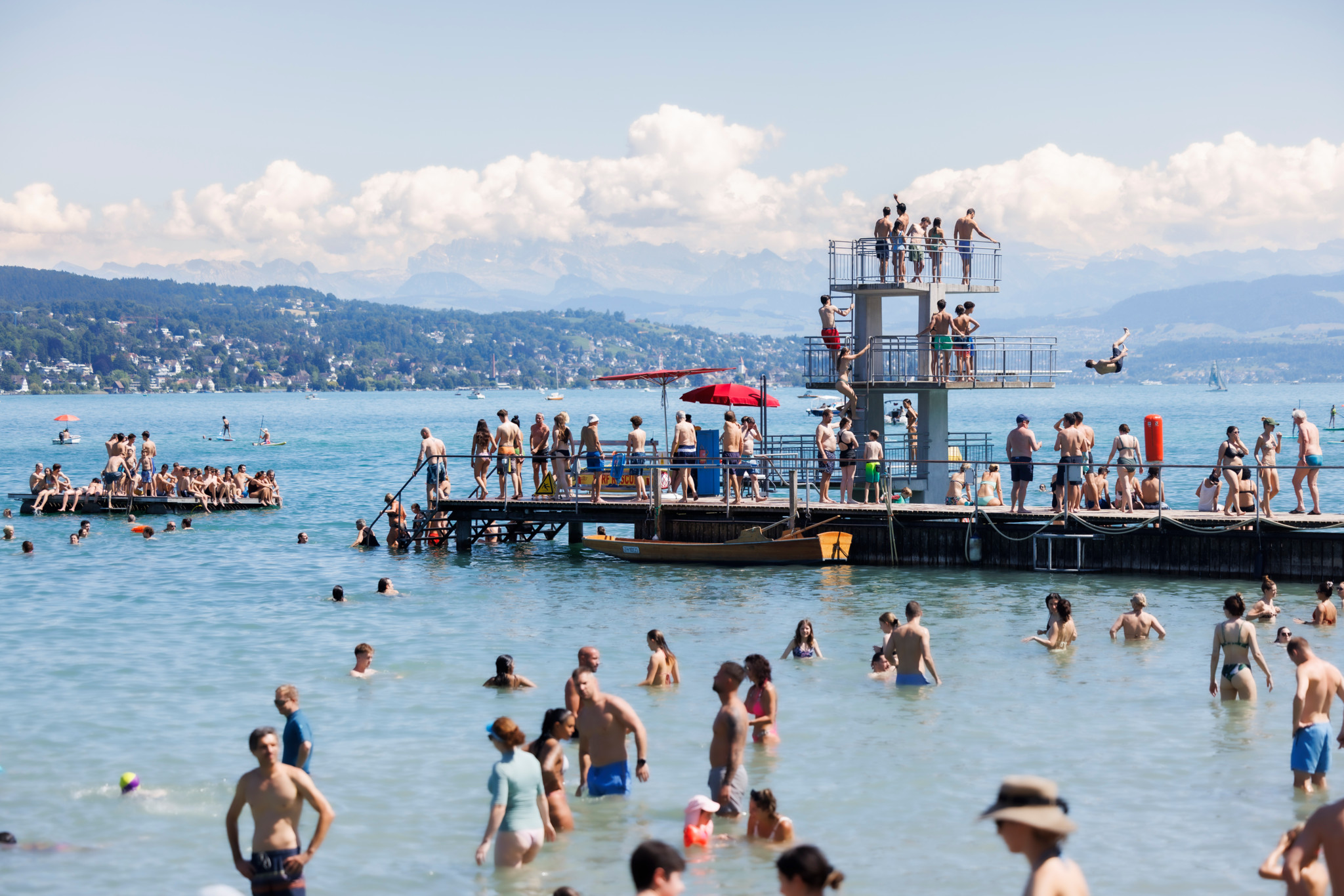 Menschen geniessen einen sonnigen Tag an der Badi Mythenquai in Zürich mit Turmspringen und Schwimmen im Zürichsee.